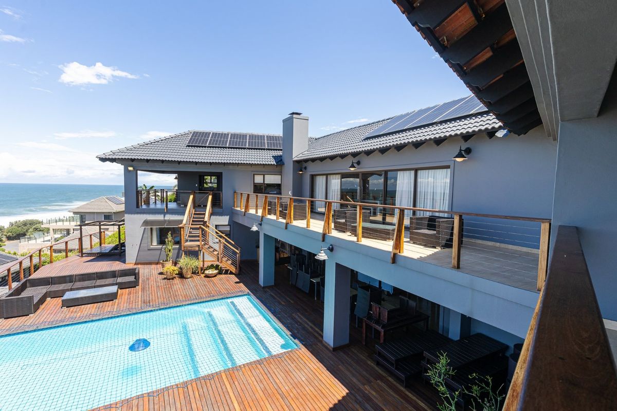 A spacious rear exterior featuring a swimming pool, extensive timber decking, a large balcony, and solar panels, offering a well-maintained outdoor entertainment area.
