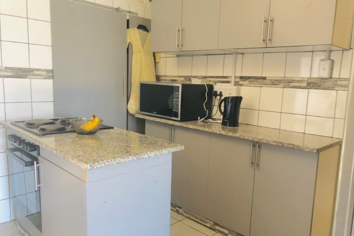 A functional kitchen featuring grey cabinetry, granite countertops, a built-in oven, and an electric hob with a tiled backsplash.