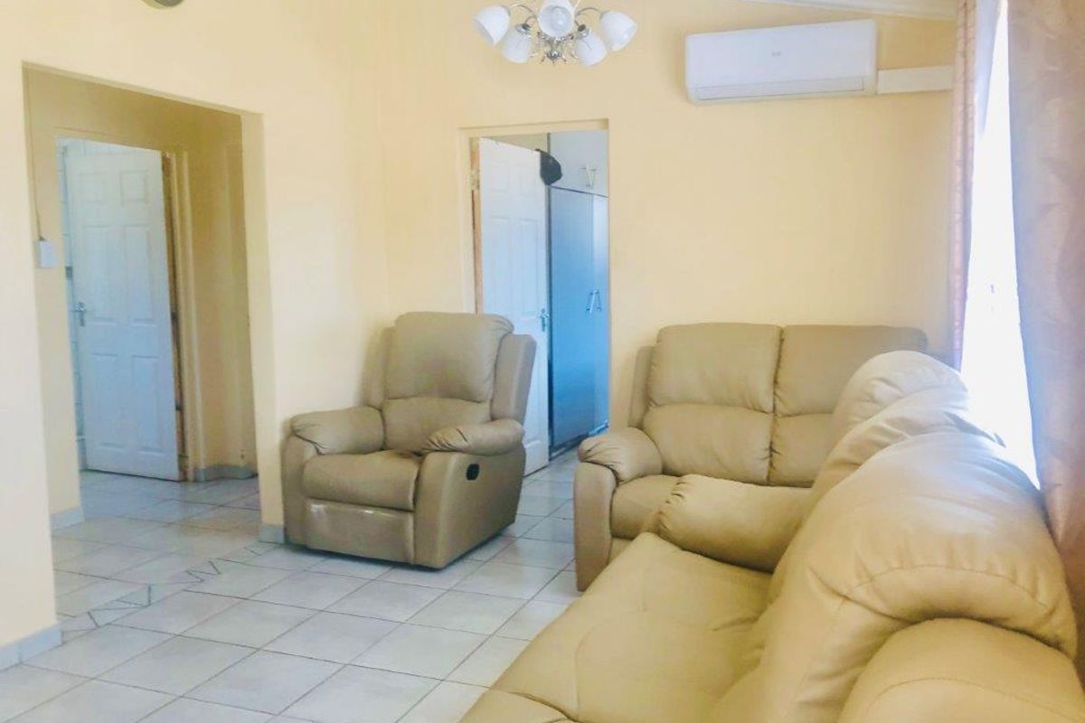A living room featuring tiled flooring, a split-system air conditioner, and a central chandelier, providing a functional and neutral living space.