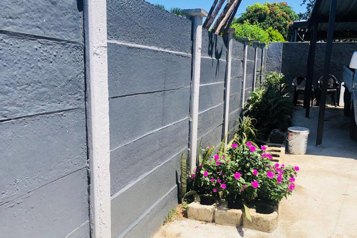A view of a rear outdoor area featuring a painted precast concrete boundary wall and concrete paving.