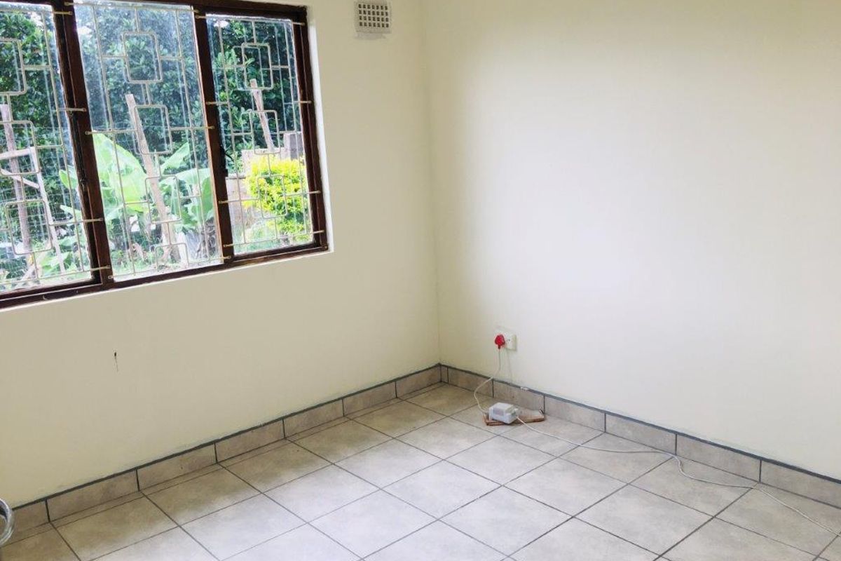 A clean, empty bedroom featuring neutral tiled flooring, security burglar bars on the window, and standard electrical fixtures.