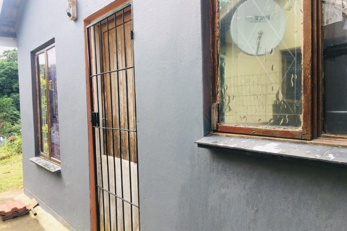 Exterior view of the rear building facade featuring timber window frames, a security gate, and concrete sills showing signs of wear.