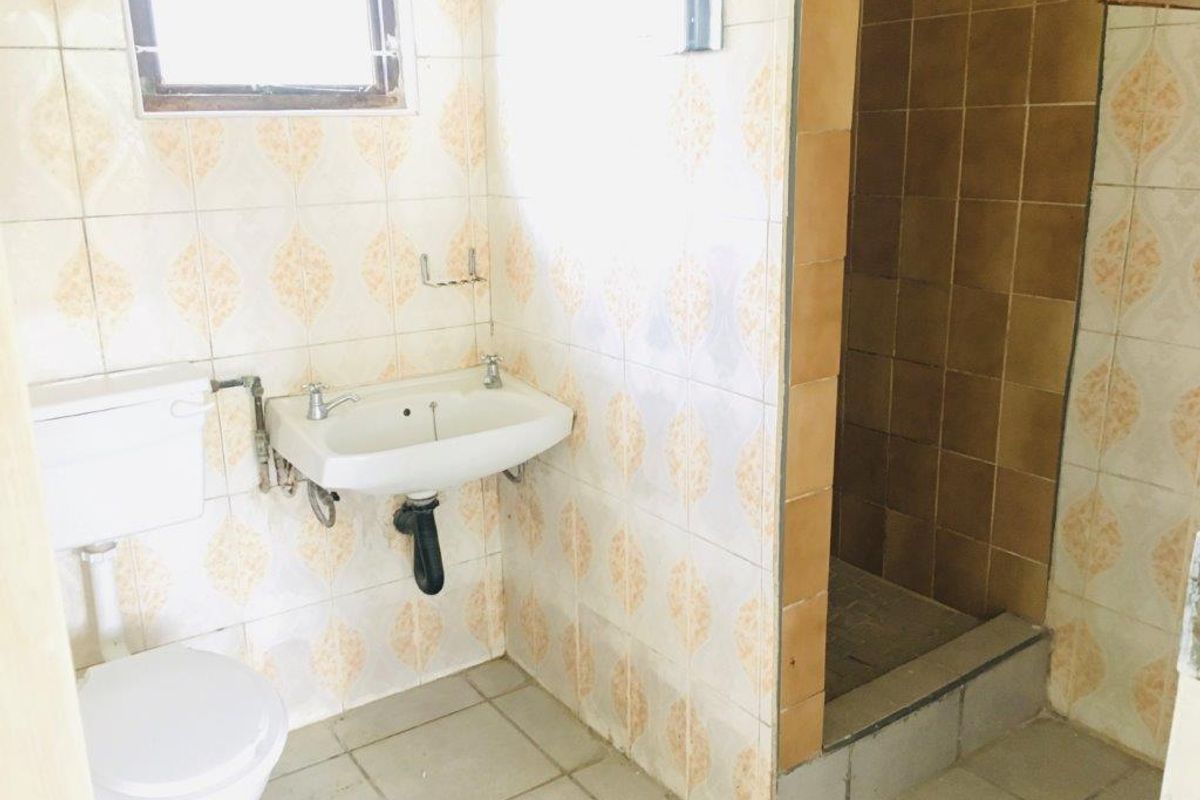 A dated bathroom featuring a wall-mounted basin, toilet, and a separate shower enclosure with tiled finishes throughout.