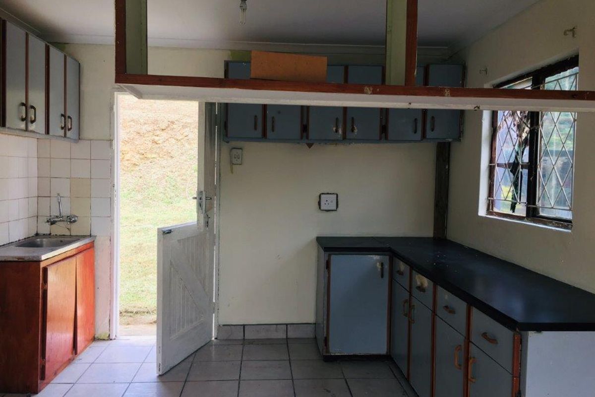 A dated kitchen featuring built-in cabinetry, tiled flooring, and direct access to the rear exterior, offering significant potential for modernization and renovation.