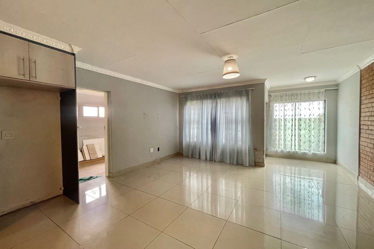 Spacious living area featuring large format floor tiles, an exposed brick feature wall, and built-in cabinetry, offering a blank canvas for interior design.