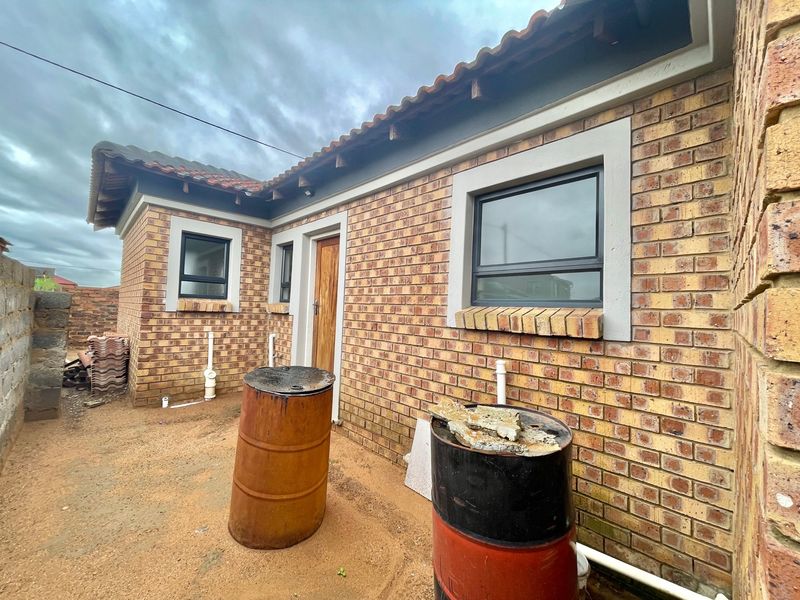 Rear exterior view of a face brick house featuring tiled roofing, aluminium window frames, and unfinished ground area.