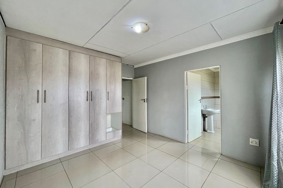 A spacious bedroom featuring built-in cupboards, tiled flooring, and direct access to an en-suite bathroom.