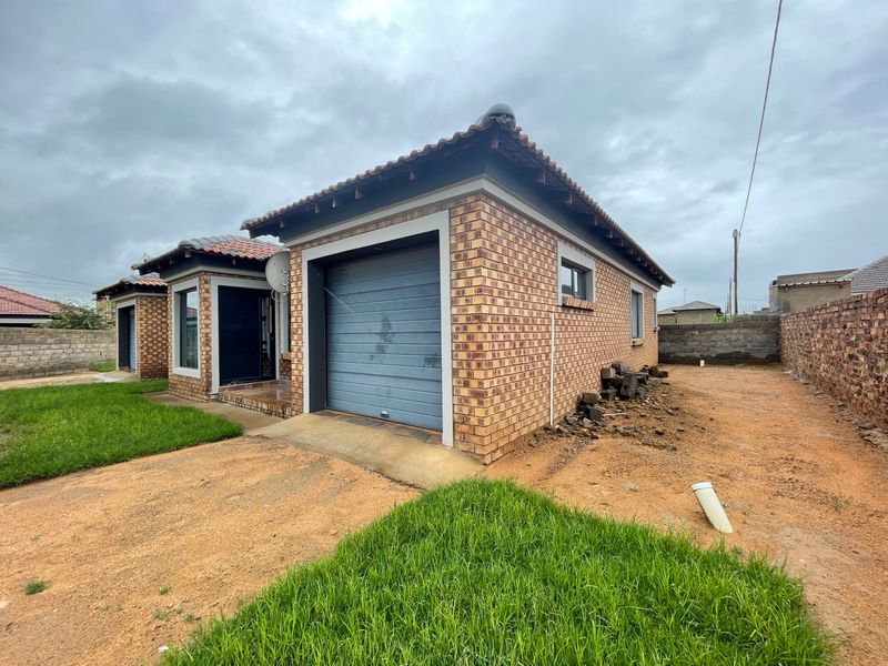 Front view of a face brick house featuring a single garage, tiled roof, and an unlandscaped yard area.