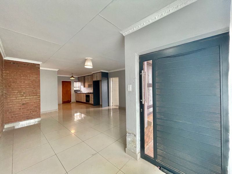 Spacious open-plan living area featuring tiled floors, an exposed brick feature wall, and a functional kitchen with built-in cabinetry and appliances.