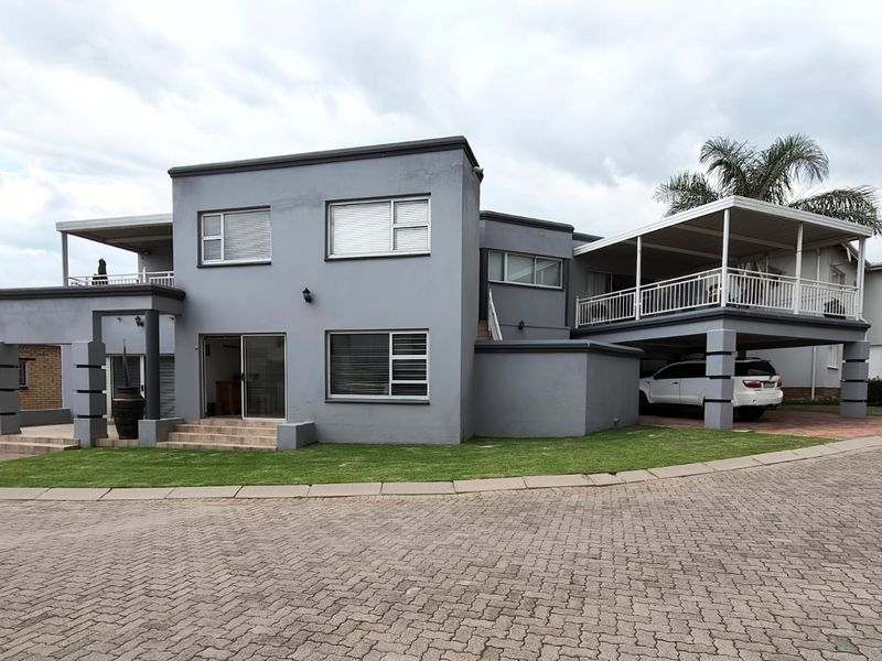 A modern two-story house exterior featuring a grey facade, covered patio, balcony, and a paved driveway with integrated carport parking.