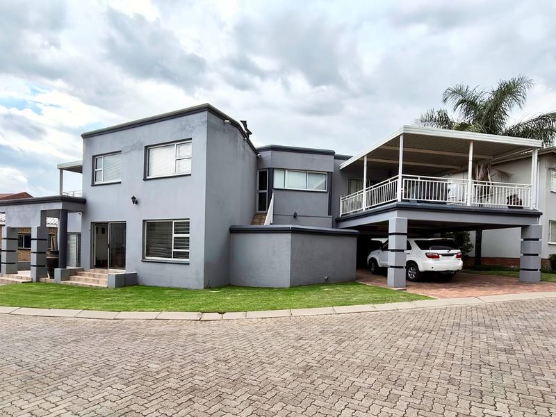 A modern two-story residential property featuring a paved driveway, integrated carport, and an upper-level balcony with metal railings.