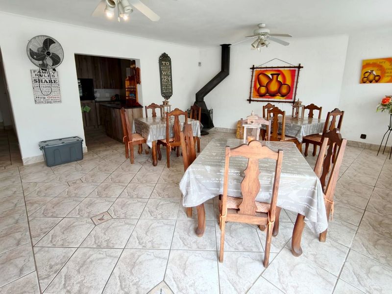 Open-plan living and dining area featuring tiled flooring, a freestanding fireplace, and ceiling fans, with an adjacent kitchen space.