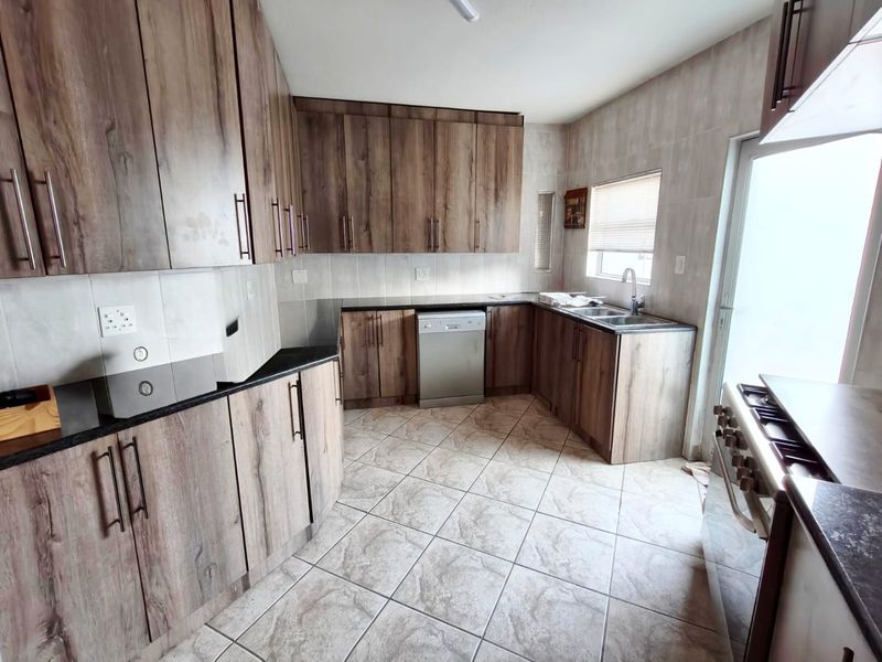 A functional kitchen featuring wood-look cabinetry, tiled flooring, a double sink, and built-in appliances including a dishwasher and gas stove.