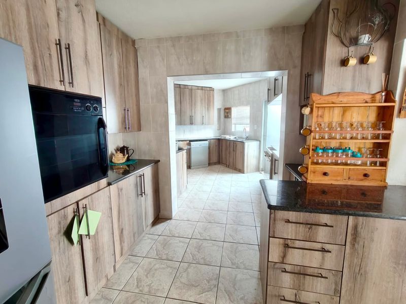 A functional kitchen featuring wood-look cabinetry, granite countertops, tiled flooring, and a separate scullery area with additional storage and sink.