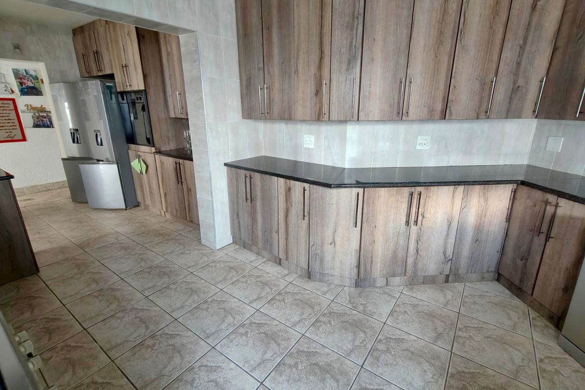 A functional kitchen featuring wood-look cabinetry, dark granite countertops, tiled flooring, and a built-in oven with an adjacent scullery area.