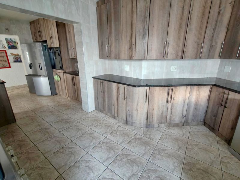 A functional kitchen featuring wood-look cabinetry, dark granite countertops, tiled flooring, and a built-in oven with an adjacent scullery area.