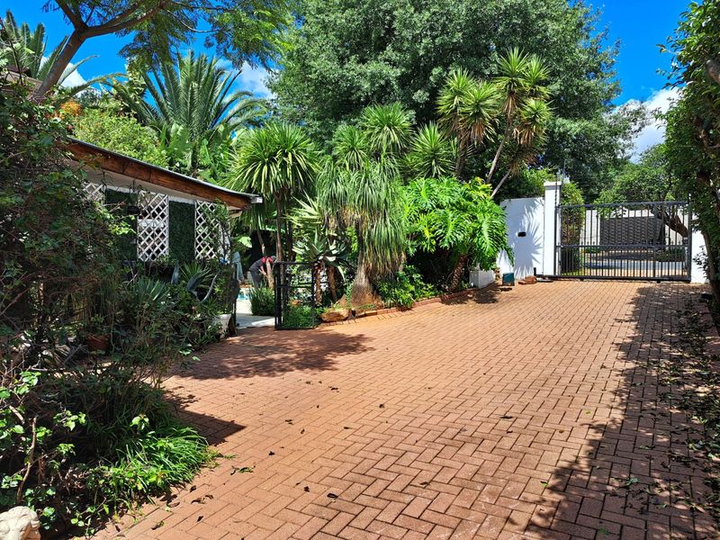 A paved driveway leading to a secure gated entrance, featuring mature garden landscaping and a lattice-screened side structure.