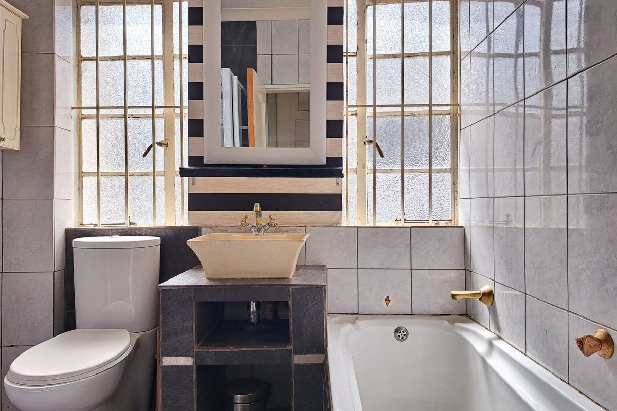 A dated bathroom featuring a vessel sink on a tiled vanity, a standard bathtub, and tiled walls with security bars on the windows.