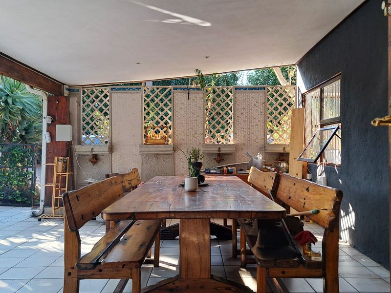 A covered outdoor patio area featuring tiled flooring, decorative lattice wall panels, and recessed ceiling lighting, providing a functional space for outdoor dining.