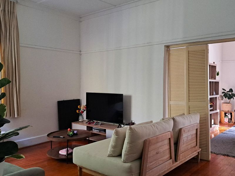 A living room featuring original timber flooring, picture rails, and louvered folding doors connecting to an adjacent dining area.