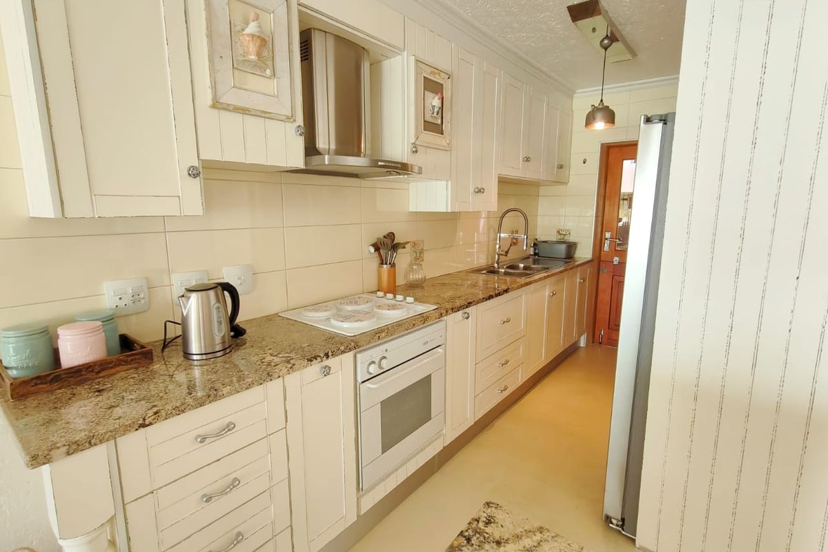 A functional galley-style kitchen featuring granite countertops, shaker-style cabinetry, built-in oven, electric hob, and a stainless steel extractor fan.