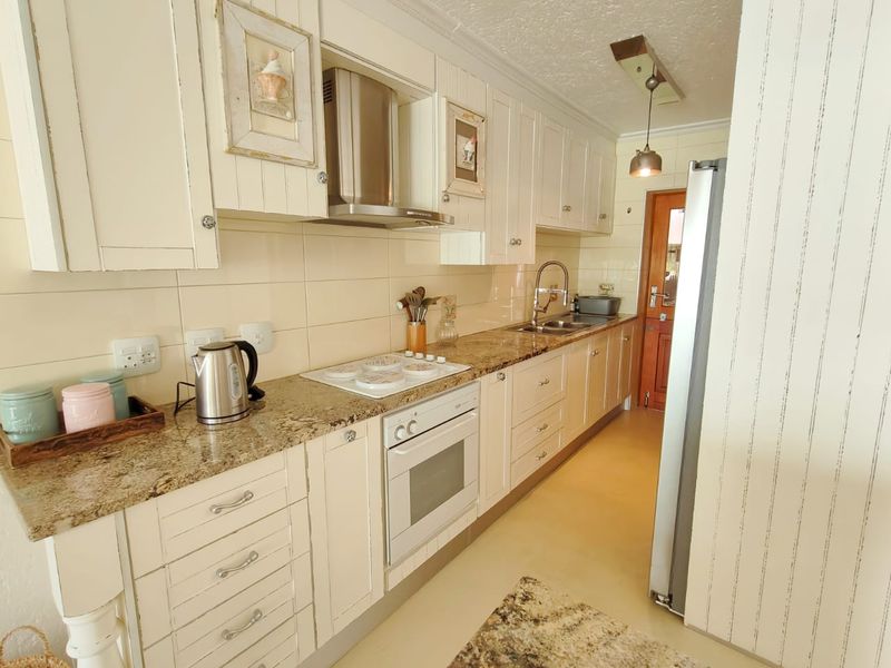 A functional galley-style kitchen featuring granite countertops, shaker-style cabinetry, built-in oven, electric hob, and a stainless steel extractor fan.