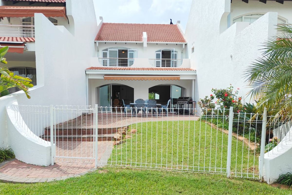 Rear view of a townhouse featuring a private garden, paved patio area with a retractable awning, and an upper-level balcony with sliding glass doors.