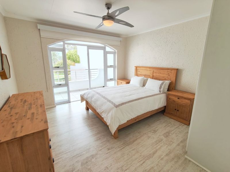 A bright bedroom featuring laminate flooring, a ceiling fan, and a large sliding glass door providing access to an outdoor balcony.