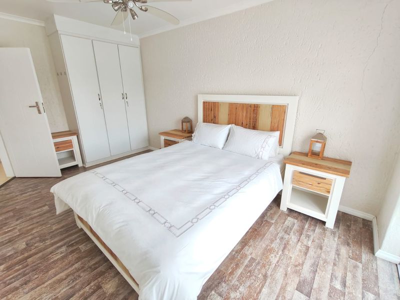 A well-lit bedroom featuring built-in wardrobes, a ceiling fan, and wood-look laminate flooring, offering a functional and comfortable living space.