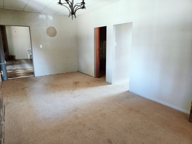 An empty living room featuring a drop ceiling, chandelier, and a wood-burning stove, requiring cosmetic updates to the flooring and wall finishes.