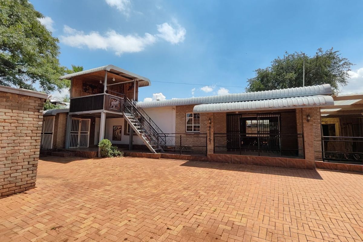 Rear exterior view featuring brick paving, a raised timber deck with a metal staircase, and covered patio areas with security gates.