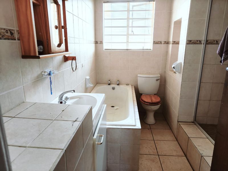 A functional bathroom featuring a built-in bathtub, separate shower enclosure, pedestal basin, and toilet, finished with neutral ceramic wall and floor tiles.
