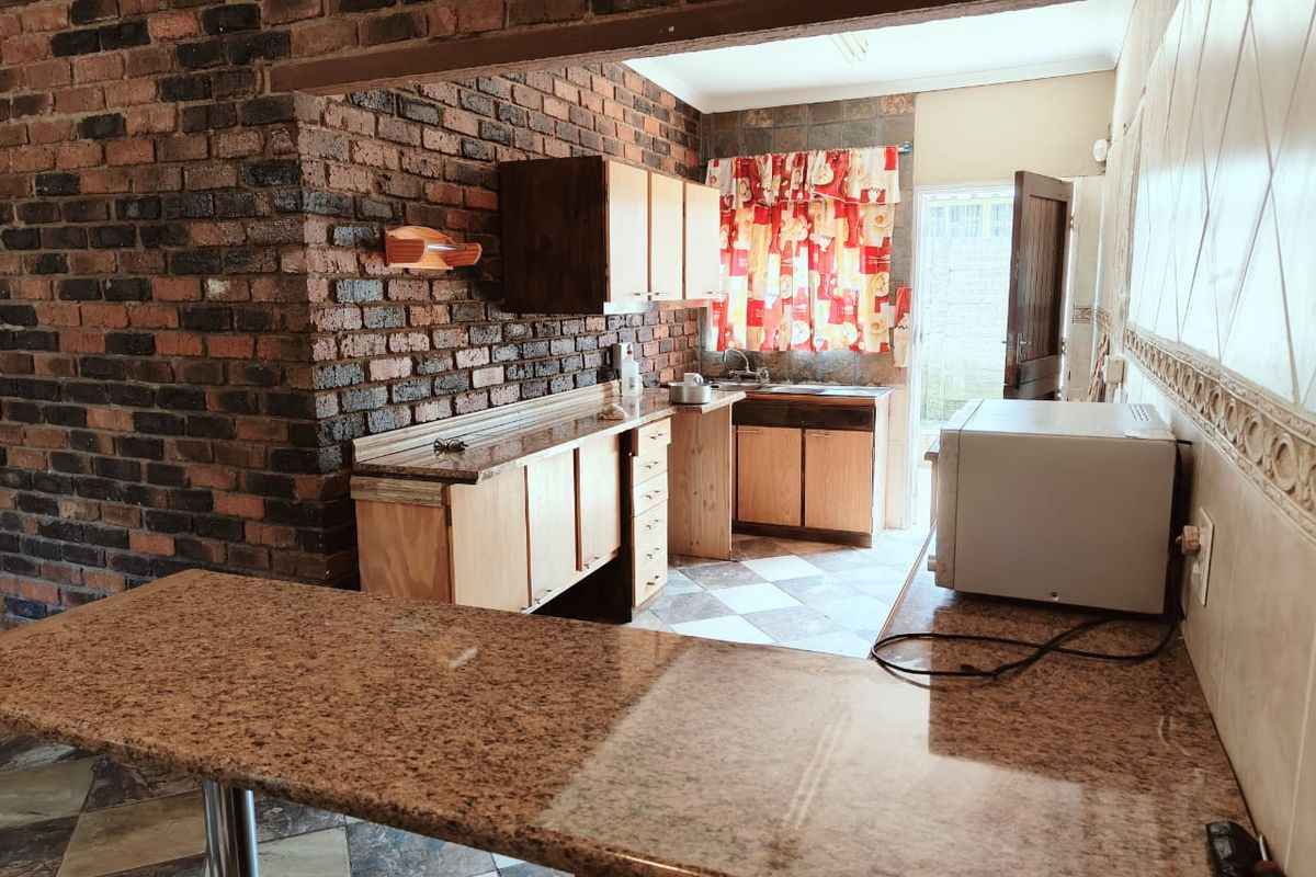 A functional kitchen featuring exposed brick walls, granite countertops, wooden cabinetry, and a breakfast bar, offering a rustic aesthetic with potential for modernization.