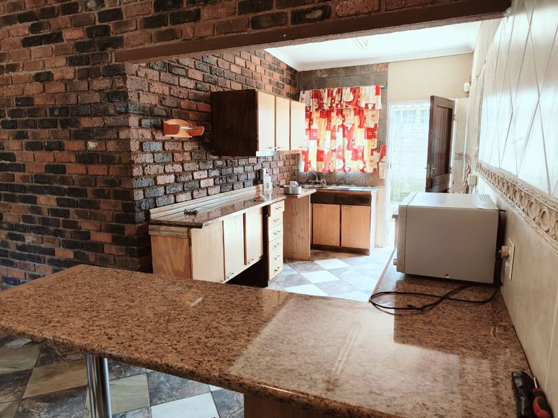 A functional kitchen featuring exposed brick walls, granite countertops, wooden cabinetry, and a breakfast bar, offering a rustic aesthetic with potential for modernization.