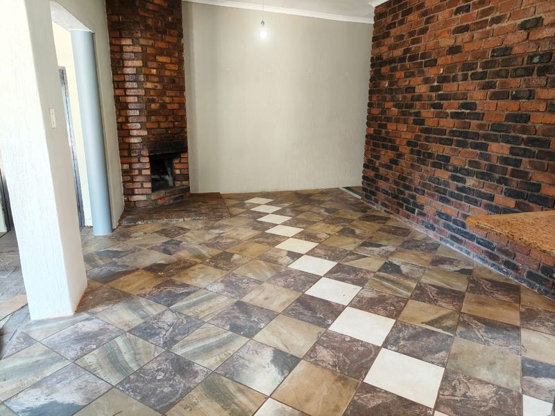 An empty living room featuring a prominent brick fireplace, exposed brick feature wall, and patterned tiled flooring.