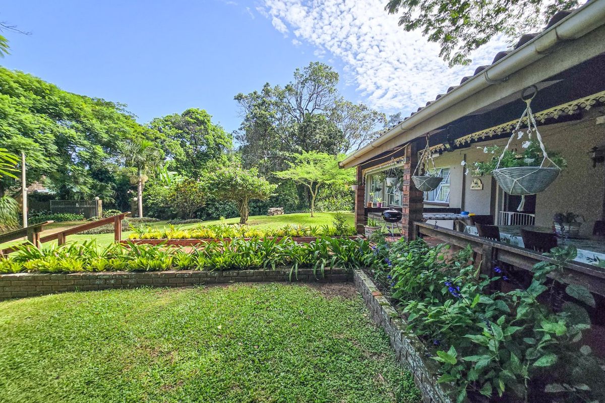 A well-maintained rear garden featuring a brick retaining wall, lush lawn, and a covered patio area with timber railings.