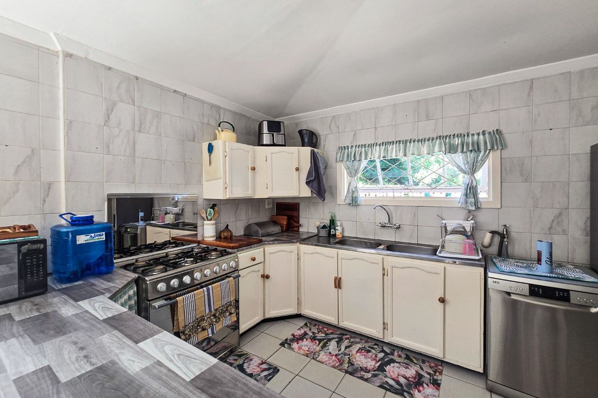 A functional kitchen featuring a gas stove, double sink, tiled splashbacks, and ample built-in cabinetry with a neutral aesthetic.
