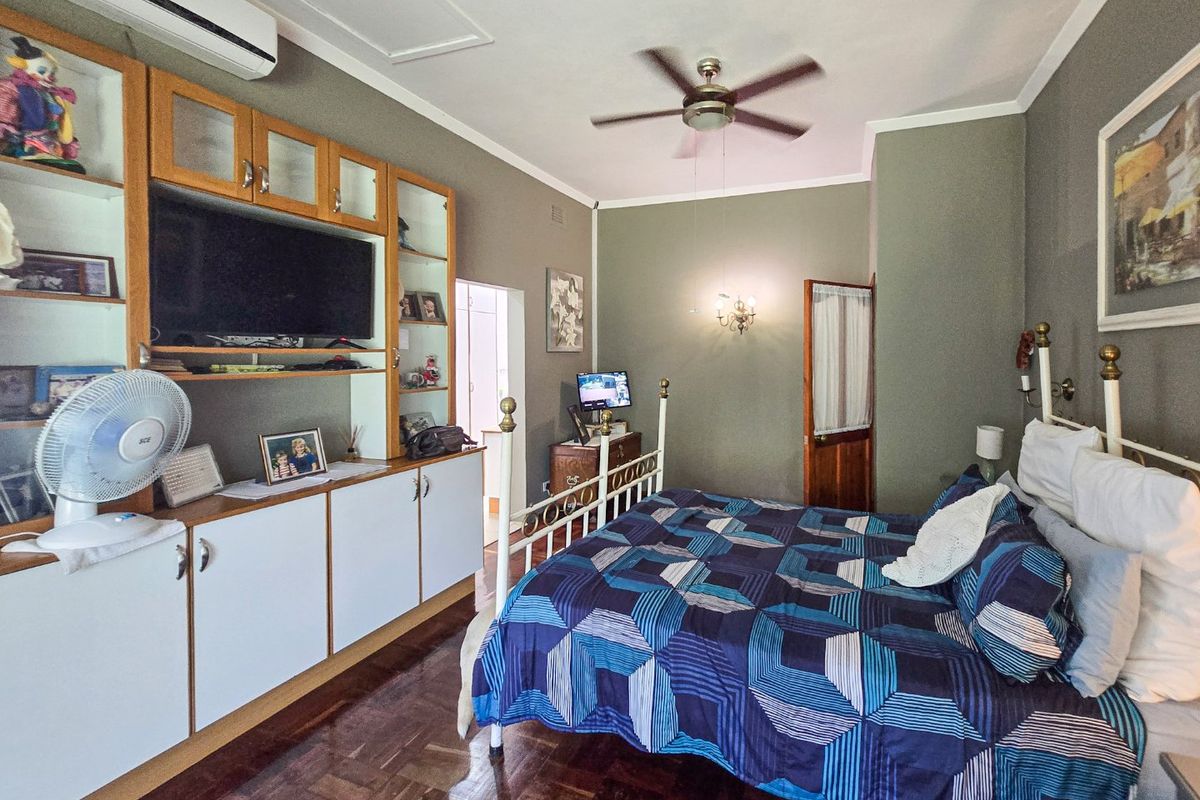 A spacious bedroom featuring parquet flooring, built-in cabinetry, a ceiling fan, and a split-system air conditioner for climate control.