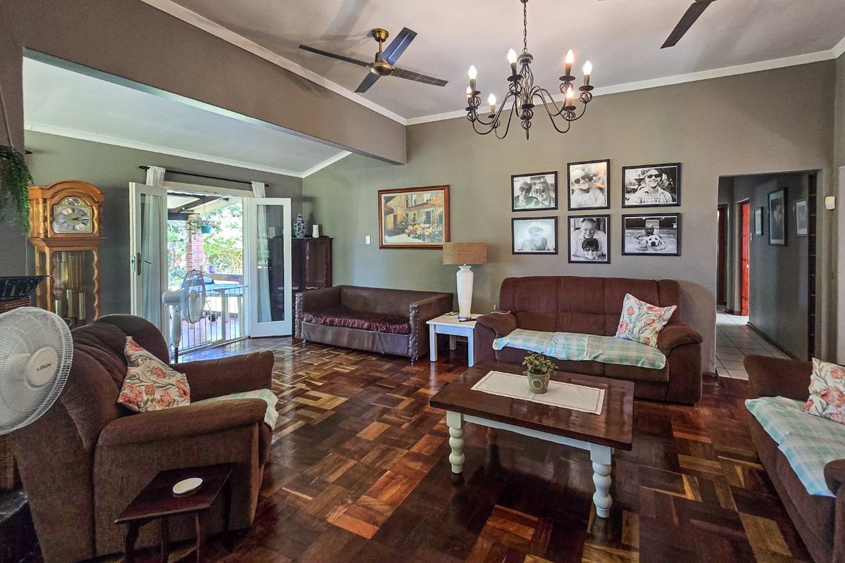 Spacious living room featuring classic parquet flooring, coved cornicing, ceiling fans, and a decorative wrought iron chandelier, with direct access to the patio.