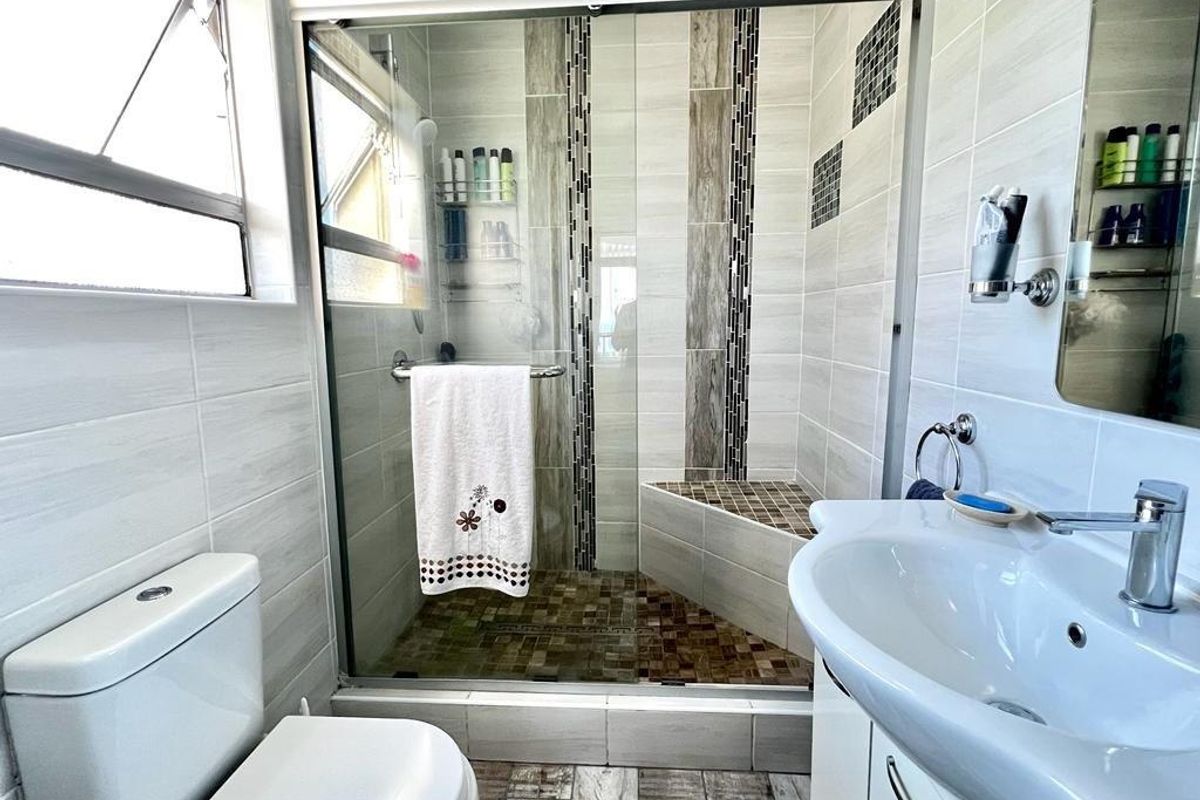 A modern bathroom featuring a walk-in shower with a built-in bench, glass enclosure, pedestal vanity, and neutral ceramic tiling throughout.