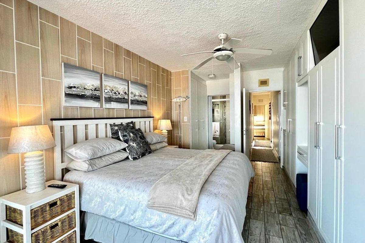A well-maintained bedroom featuring wood-look wall paneling, built-in cupboards, a ceiling fan, and tiled flooring, with an adjoining en-suite bathroom.