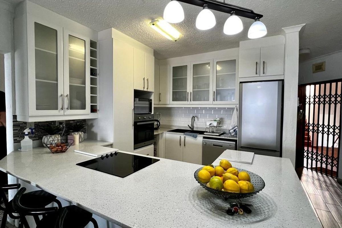 Modern kitchen featuring white cabinetry, quartz countertops, subway tile backsplash, and integrated appliances, including a built-in oven and microwave with a breakfast bar.