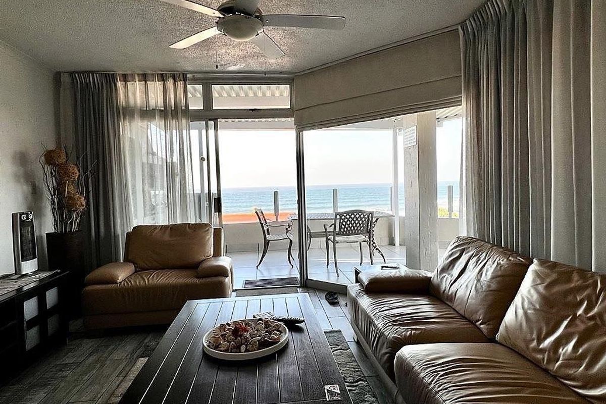 Spacious living room featuring large sliding glass doors that open to a balcony with direct ocean views and natural light.