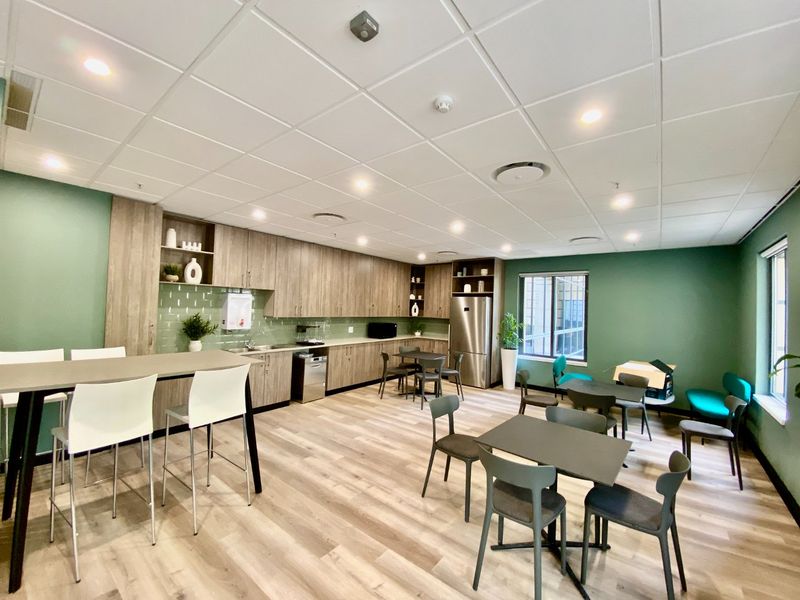 A modern commercial kitchen and breakroom area featuring wood-finish cabinetry, integrated appliances, subway tile backsplash, and a suspended ceiling with recessed lighting.