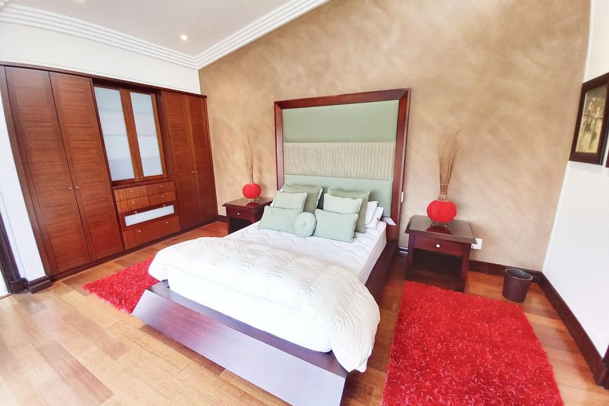 Spacious bedroom featuring warm hardwood flooring, extensive built-in wooden cabinetry, and elegant crown molding with recessed lighting.
