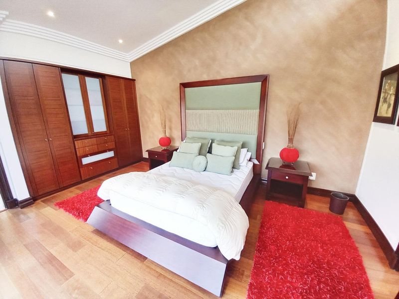 Spacious bedroom featuring warm hardwood flooring, extensive built-in wooden cabinetry, and elegant crown molding with recessed lighting.