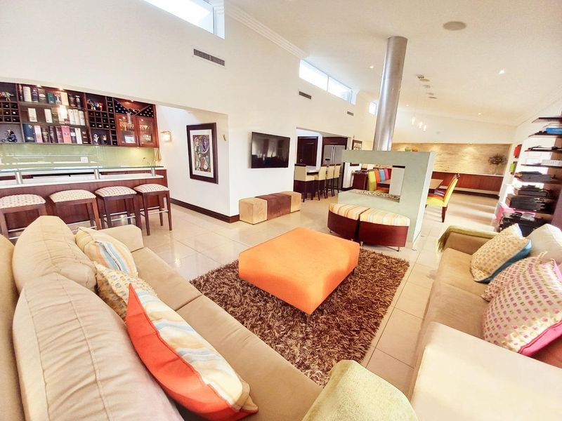 Spacious open-plan living area featuring a built-in bar, double-sided fireplace, high ceilings with clerestory windows, and polished tile flooring.