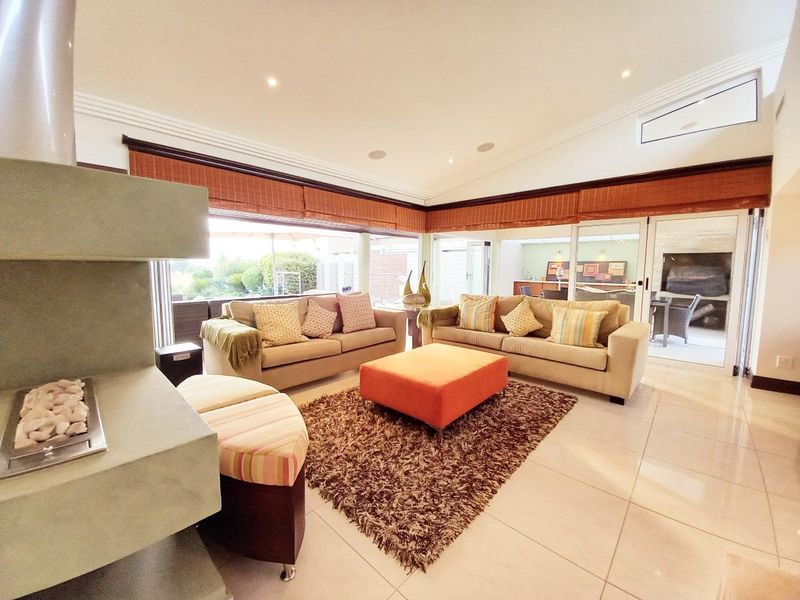 Spacious living room featuring a modern fireplace, vaulted ceilings, recessed lighting, and large sliding glass doors that provide seamless access to the outdoor patio area.