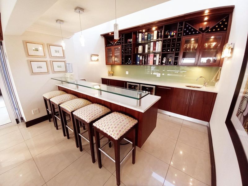 A well-appointed home bar featuring custom dark wood cabinetry, glass shelving, integrated wine storage, a sleek glass-topped bar counter, and modern tile flooring.