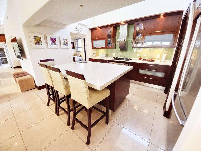 Modern kitchen featuring a central island with stone countertops, dark wood cabinetry, glass splashback, and integrated gas hob with extractor fan.